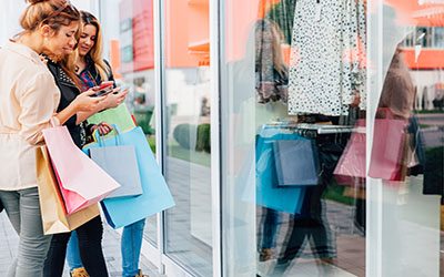 Teens looking at mobile phone model of clothes in front of shopping windows